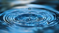 Macro photography of water drops falling into calm surface creating concentric ripple patterns in deep blue tones, capturing moment of impact and splash formation.