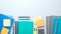 Colorful office supplies and stationery items arranged on white background including notebooks, calculator, sticky notes and pens for workspace organization.