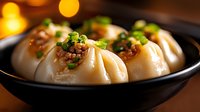 Steamed Asian dumplings with minced meat filling garnished with chopped green onions and spices in black ceramic bowl against warm bokeh background.