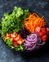 Fresh colorful salad bowl with kale, shredded carrots, cherry tomatoes and red onions on dark background for healthy eating and nutrition concepts.