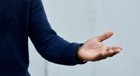 Male hand in navy blue knitted sweater extended in open gesture showing palm upward for presentation or offering concept against neutral background.