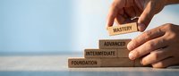 Hands building wooden block pyramid with skill levels from foundation to mastery representing career development and professional growth concept.
