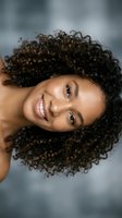 Happy young African American woman with curly hair smiling joyfully at camera against soft blurred background for lifestyle and wellness content.