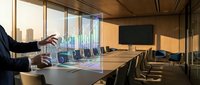 Modern conference room with businessman presenting holographic data visualization during corporate meeting with city skyline view through windows.