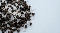 Black and white peppercorns with coarse sea salt crystals scattered on clean surface for culinary seasoning and cooking applications.