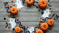 Halloween decorations arranged in circle on rustic wooden background with orange pumpkins, white paper ghosts, black ribbons and stars for autumn holiday celebration.