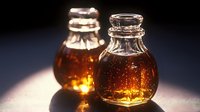 Amber glass bottles with golden liquid glowing in warm light, vintage apothecary style containers for aromatherapy, essential oils, or herbal remedies.