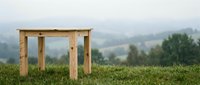 Wooden table frame standing alone on green grass with misty mountain landscape and forest in background, suitable for outdoor furniture design and nature-themed projects.