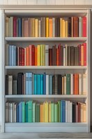 Colorful books arranged by spectrum on white wooden bookshelf creating rainbow effect. Collection of hardcover volumes organized aesthetically for home library or study.