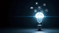 Light bulb with brain inside and technology icons floating above on dark blue background representing artificial intelligence and innovation concepts.