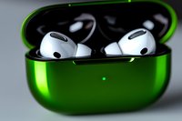 White wireless earbuds in metallic green charging case with LED indicator light, close-up view showing glossy finish and premium design details on neutral background.
