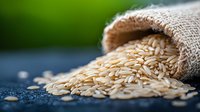 Organic brown rice grains spilling from burlap sack on dark surface with green background for healthy cooking and nutrition concepts.