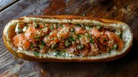 Fresh salmon tartare served in crusty baguette with herbs and seasonings on rustic wooden background, gourmet seafood sandwich preparation.
