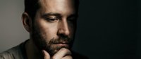 Thoughtful bearded man in contemplative pose with hand on chin against dark background for business and lifestyle concepts.