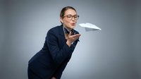 Caucasian male professional in dark business suit and eyeglasses throwing paper airplane, representing innovation, entrepreneurship, and forward-thinking business strategy for corporate communications.
