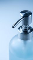 Modern chrome soap dispenser with frosted glass bottle on clean blue background for bathroom and kitchen hygiene concepts.