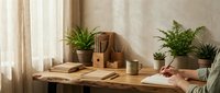 Cozy home office workspace with wooden desk, green plants, notebooks and coffee mug creating productive work from home environment for modern lifestyle.