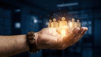 Businessman holding glowing people icons in palm against blurred office background, representing team management, human resources, networking, and digital leadership concepts.
