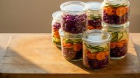 Colorful fermented vegetables in glass jars on wooden cutting board. Homemade pickled cabbage, carrots, cucumbers for healthy probiotic nutrition and preservation.
