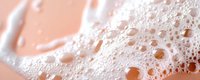 Macro shot of soap foam bubbles in soft pink and white tones creating abstract texture pattern with water droplets and light reflections. For beauty and hygiene concepts.
