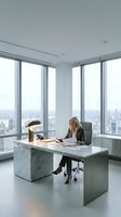 Mature woman with long blonde hair, wearing dark blazer, seated at marble desk in high-rise office with panoramic city skyline views through floor-to-ceiling windows, working on laptop and documents.