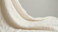 Soft cream colored knitted wool fabric with cable pattern draping elegantly, showcasing natural textile texture for cozy home decor and fashion design projects.