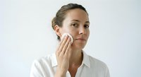 Professional woman applying skincare cream to face with cotton pad for daily beauty routine and facial care regimen.