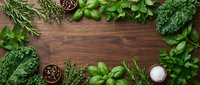Fresh green herbs and leafy vegetables arranged as border frame on rustic wooden background with copy space for culinary and cooking concepts.