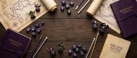 Flat lay of tabletop RPG accessories on dark wood, featuring dice, maps, journals, and pencils arranged around a central copy space.