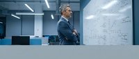 Mature businessman analyzing data on whiteboard in modern office environment. Strategic planning and business intelligence concept for corporate presentations.
