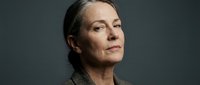 Mature woman with gray hair pulled back, fair complexion, wearing neutral beige sweater against gray background. Professional headshot suitable for corporate, business, and editorial use.