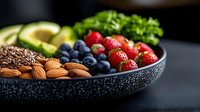 Fresh healthy ingredients in dark bowl including strawberries, blueberries, almonds, flax seeds, avocado and leafy greens on black background for clean eating.