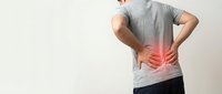 Man suffering from lower back pain holding his spine with red highlight indicating inflammation or injury on neutral background.