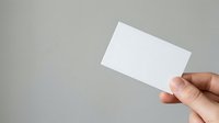 Person with medium skin tone holding blank white business card against neutral gray background for branding and corporate identity mockup purposes.