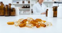 Pharmaceutical capsules and pills scattered on laboratory table with pharmacist working in background preparing medications for healthcare treatment.