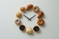 Creative clock made from assorted donuts and pastries arranged in circle with black hands on white background for food time concept design.