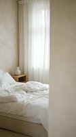 Minimalist bedroom interior with unmade white bedding and sheer curtains creating soft natural light for peaceful morning atmosphere and home decor concepts.