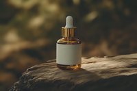 Glass dropper bottle with golden serum on natural stone surface against blurred forest background, minimalist organic skincare concept in warm tones.
