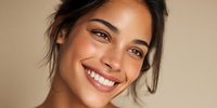 Happy young Hispanic woman with radiant smile and glowing skin showing natural beauty and positive emotions against neutral beige background for wellness concepts.