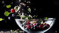 Fresh berries and green leaves falling into glass bowl with water splash against dark background, dramatic food photography with motion capture.