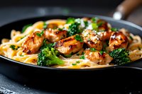 Creamy fettuccine pasta with grilled chicken pieces and steamed broccoli florets in rich alfredo sauce, garnished with fresh herbs and black pepper.