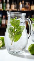Glass pitcher filled with sparkling water, fresh mint leaves and lime slices on bar counter. Refreshing mojito mocktail preparation in restaurant setting.