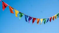 Colorful bunting flags strung across clear blue sky, festive decoration for parties, celebrations, weddings, and outdoor events.