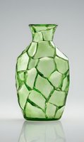 Green glass vase with geometric crackle pattern texture on gray background with reflection, modern decorative home accent piece for interior design.