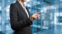 Professional businesswoman in dark suit interacting with futuristic holographic interface displaying digital data and analytics in modern office environment.