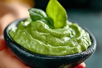 Fresh avocado guacamole dip garnished with basil leaf served in stone mortar, close up view of creamy Mexican appetizer with smooth texture.