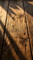 Weathered wooden planks with natural grain texture and warm sunlight shadows creating rustic background surface for product photography and design projects.