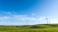Wind turbines dotting rolling green hills under bright blue sky with white clouds, representing renewable energy and sustainable power generation for environmental projects.