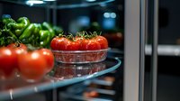 Fresh cluster tomatoes on vine in modern refrigerator, close up view showing ripe red and green produce on glass shelf with soft lighting and bokeh effect.