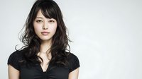 Young Asian woman with long dark wavy hair and bangs wearing black top against white background, perfect for beauty, fashion, or portrait photography.